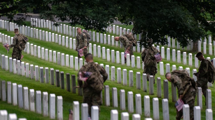 Military members place flags at the headstones of U.S. military personnel buried at Arlington National Cemetery