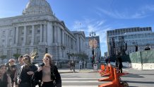 People walk across a blocked off street in San Francisco right in front of City Hall where a large stage is set up in the background.