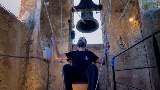 Sitting in a chair with ropes looped around both feet and hands, Joan Carles Osuna, a student of the Vall d'en Bas School of Bell Ringers, performs playing all four bronze bells at the church bell tower of the12th-century Sant Romà church, at the village of Joanetes, about two hours north of Barcelona, Spain, Saturday, June 29, 2024. A school set up to revive the manual ringing of church bells has graduated its first class of 18 students after learning their ringing skills.