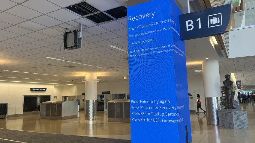 An indoor airport baggage carousel with a pillar in the middle that is covered in a blue screen displaying an error message.