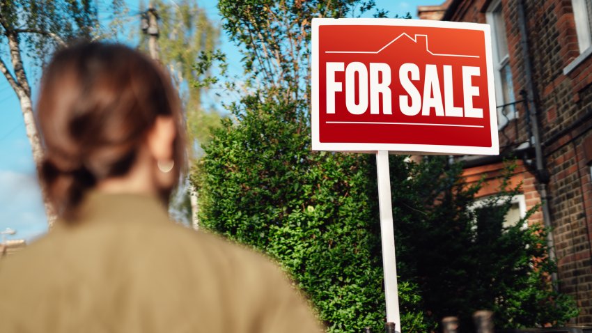 Rear view of woman looking looking at real estate sign, planning to invest in a house. Buying a new home. Property investment. Mortgage loans.