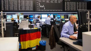 Financial traders monitor data on computer screens as the DAX Index curve sits on an electronic board beyond inside the Frankfurt Stock Exchange in Frankfurt, Germany.