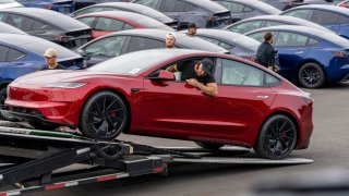 A worker unloads a new Tesla Model 3 from a truck at a logistics drop zone in Seattle, Washington, US, on Thursday, Aug. 22, 2024. 