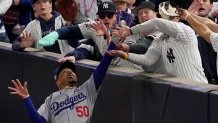 Fans interfere with a foul ball caught by Los Angeles Dodgers right fielder Mookie Betts during the first inning in Game 4 of the baseball World Series against the New York Yankees, Tuesday, Oct. 29, 2024, in New York. (AP Photo/Ashley Landis)