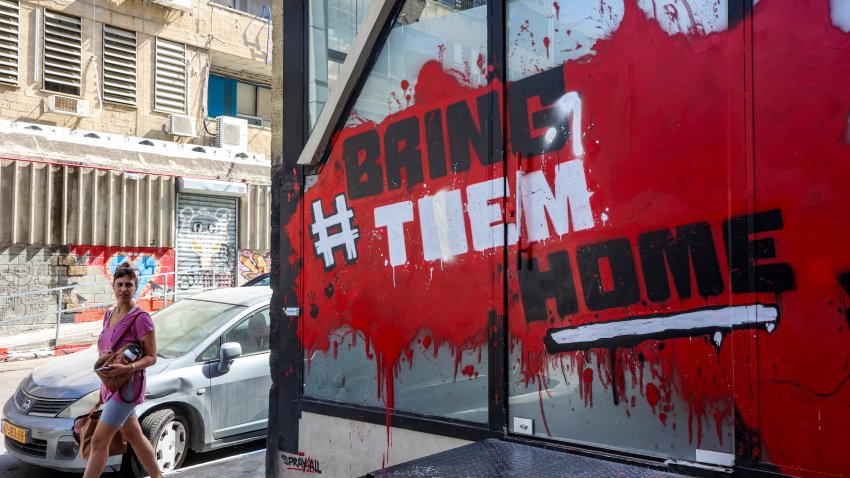 A woman walks past graffiti showing the slogan "#BringThemHome",