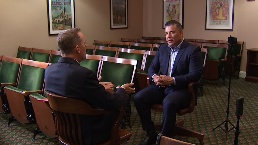 California Insurance Commissioner Ricardo Lara sits down across from NBC Bay Area Consumer Investigator Chris Chmura in a room in front of rows of green chairs.