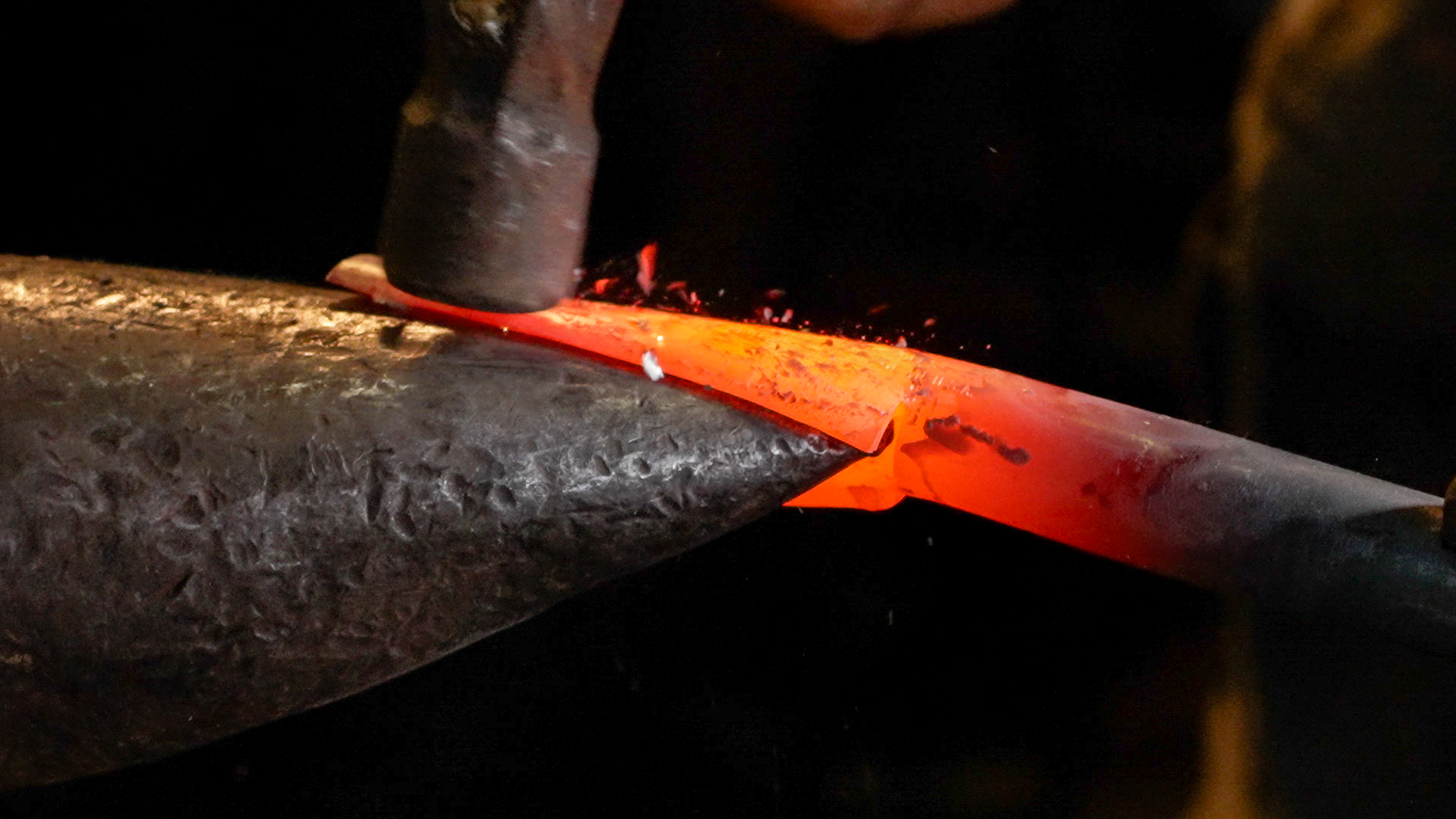 Blacksmith hammering orange glowing metal on the horn of an anvil.