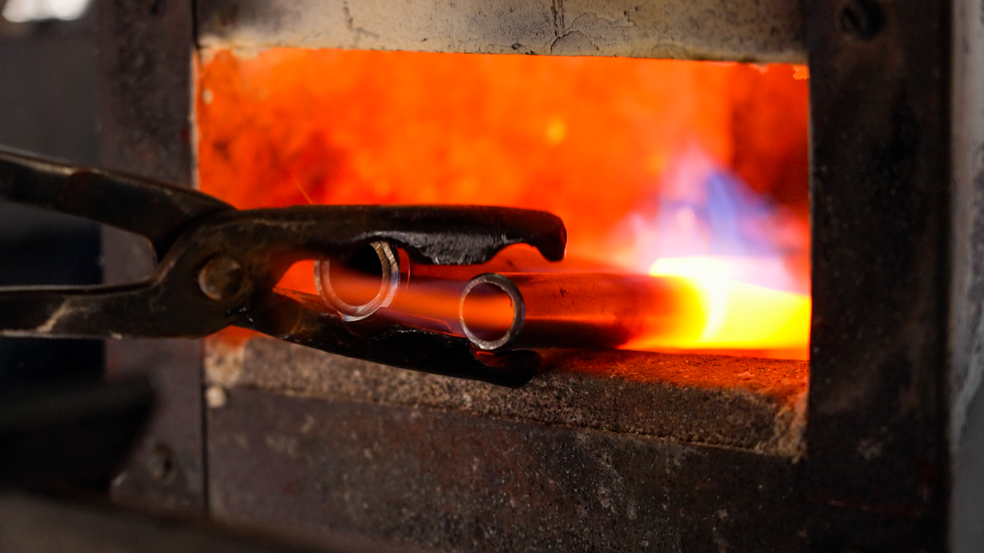 Two pieces of a gun barrel sit at the edge of a fiery red forge