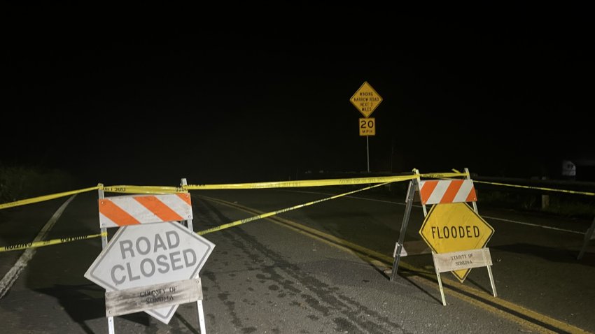 At night on an asphalt road, caution tape and flood warnig signs block off a dark road.