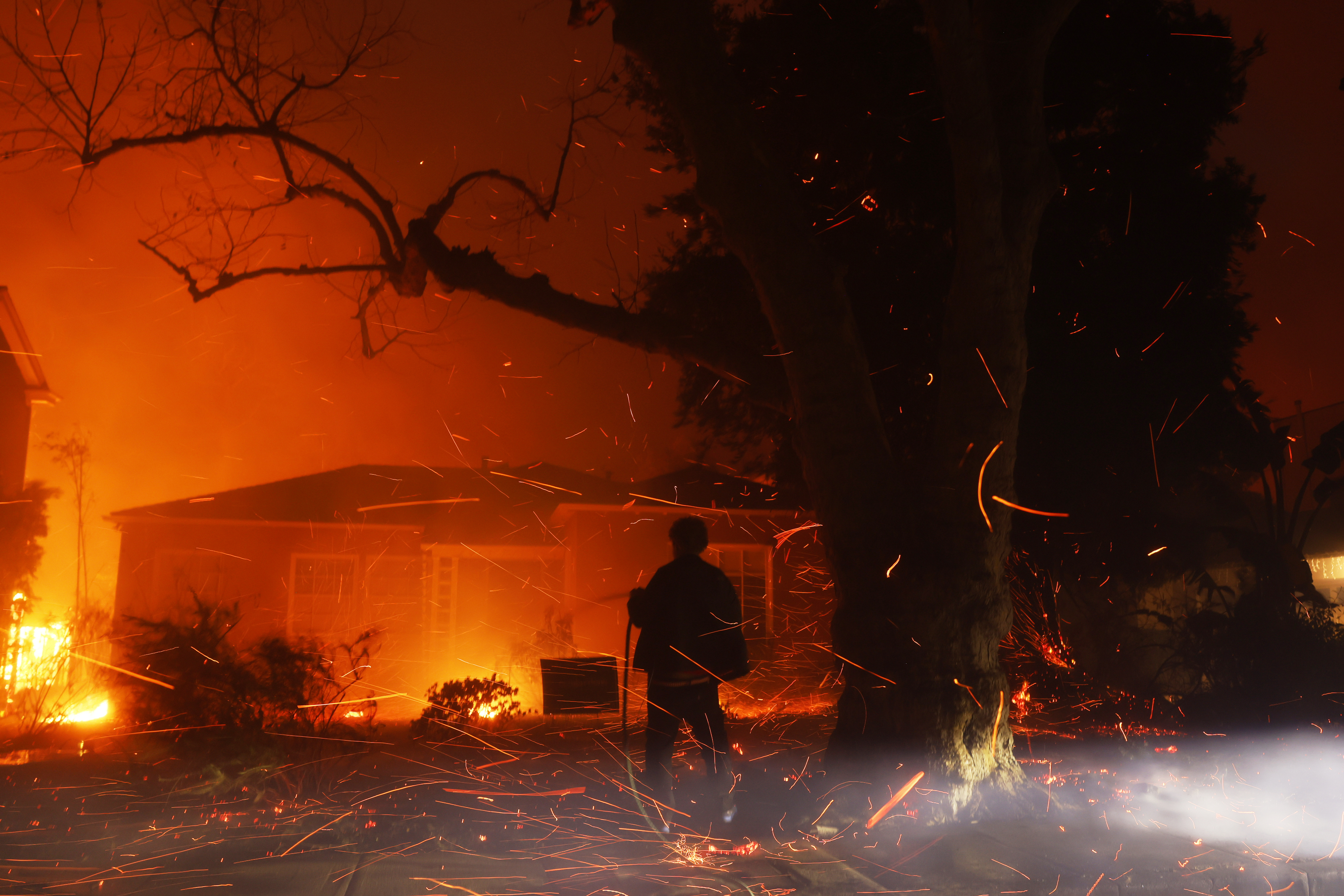 A person tries to hose down embers from the Palisades Fire in the Pacific Palisades on Jan. 7, 2025.