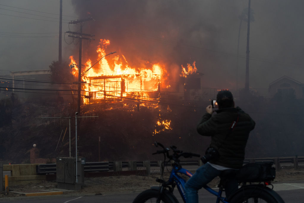 Flames from a brush fire pushed by gusting Santa Ana winds burn a home on Jan. 7, 2025 in Pacific Palisades.