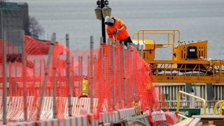 A construction worker climbs above a line of fencing at the site of a large public infrastructure reconstruction project of an elevated roadway and bridges in upper Manhattan in New York City, New York, U.S., April 22, 2021.