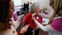 Jillian Myers, left, looks on as Ashley Manning, right, places a boutonniere on widow Linda Thompson, in honor of her husband, during a Valentine's Day Widow Outreach Project event, Thursday, Feb. 13, 2025, in Charlotte, N.C. (AP Photo/Erik Verduzco)