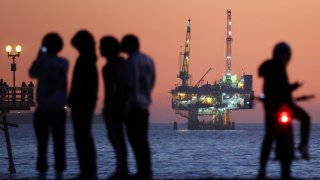 People gather at the beach after sunset with offshore oil and gas platform Esther in the distance on January 5, 2025 in Seal Beach, California.