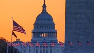 Sunrise turns the sky orange behind the U.S. Capitol building as it illuminates the U.S. Flags circling the base of the Washington Monument on March 23, 2025, in Washington, DC.