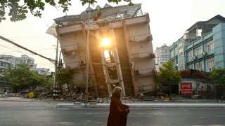 TOPSHOT – A monk walks past a collapsed building in Mandalay on April 1, 2025, a few days after the deadly Myanmar earthquake.