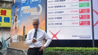 A man checks his phone next to an electronic board showing stocks on the Heng Seng Index in Hong Kong on April 3, 2025.