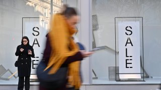 A woman stands with a coffee and looks at her phone on U.K. high street.