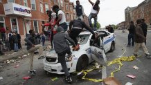 BALTIMORE, MD - APRIL 27:  Demonstrators climb on a destroyed Baltimore Police car in the street near the corner of Pennsylvania and North avenues during violent protests following the funeral of Freddie Gray April 27, 2015 in Baltimore, Maryland. Gray, 25, who was arrested for possessing a switch blade knife April 12 outside the Gilmor Homes housing project on Baltimore's west side. According to his attorney, Gray died a week later in the hospital from a severe spinal cord injury he received while in police custody.  (Photo by Chip Somodevilla/Getty Images)