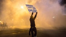 BALTIMORE, MD - APRIL 28: A protester walks through tear gas as police enforce a mandatory, city-wide curfew of 10PM near the CVS pharmacy that was set on fire yesterday during rioting after the funeral of Freddie Gray, on April 28, 2015 in Baltimore, Maryland. Gray, 25, was arrested for possessing a switch blade knife April 12 outside the Gilmor Houses housing project on Baltimore's west side. According to his attorney, Gray died a week later in the hospital from a severe spinal cord injury he received while in police custody. (Photo by Andrew Burton/Getty Images)