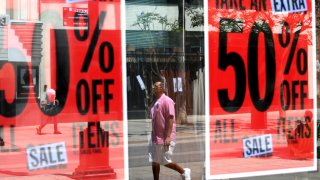 Visitors are caught in the reflection of a store offering 50% off on all items on the Third Street Promenade in Santa Monica on July 16, 2024.