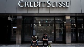 Two men sit under a sign of Credit Suisse displayed on a building in Lugano, on June 9, 2023.