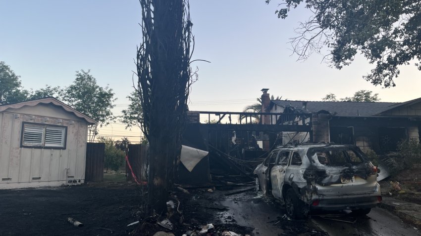 At dusk, a home and car appear burned by a recent fire that has since been put out.