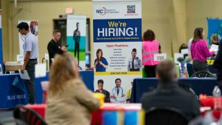 A “We’re Hiring” sign at a NC Department of Adult Correction booth at a job and resource fair hosted by the Asheville Area Chamber of Commerce in partnership with NCWorks in Fletcher, North Carolina, US, on Wednesday, April 9, 2025.