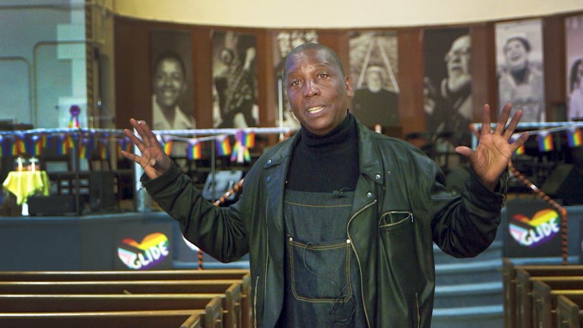 Marvin K. White stands in the sanctuary of Glide Memorial Church, flanked by Pride flags and photos of the late Cecil Williams.