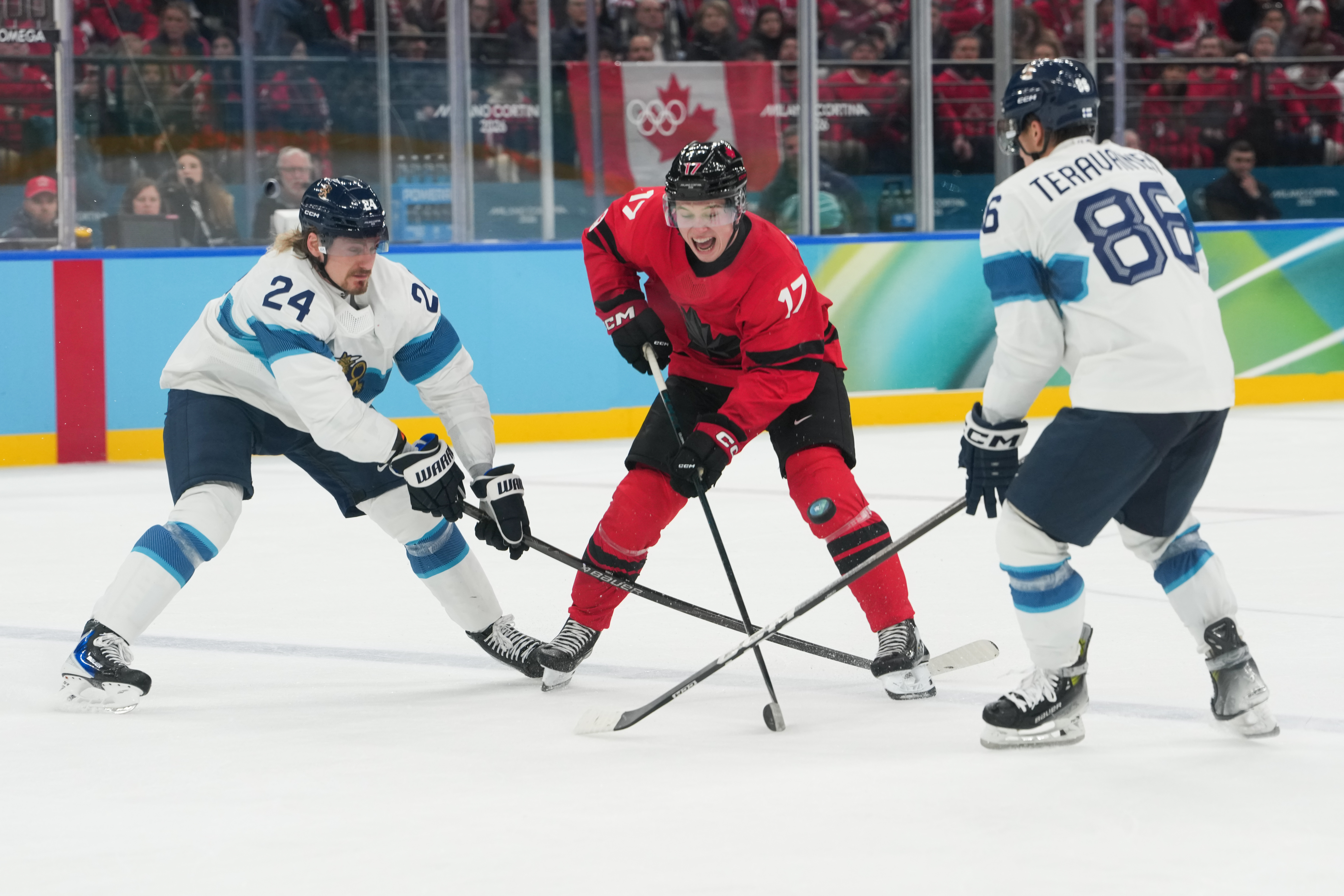 Feb 20, 2026; Milan, Italy; Macklin Celebrini (17) of Canada makes a pass as Roope Hintz (24) of Finland and Teuvo Teravainen (86) of Finland defend during the second period in a men’s ice hockey semifinal during the Milano Cortina 2026 Olympic Winter Games at Milano Santagiulia Ice Hockey Arena.