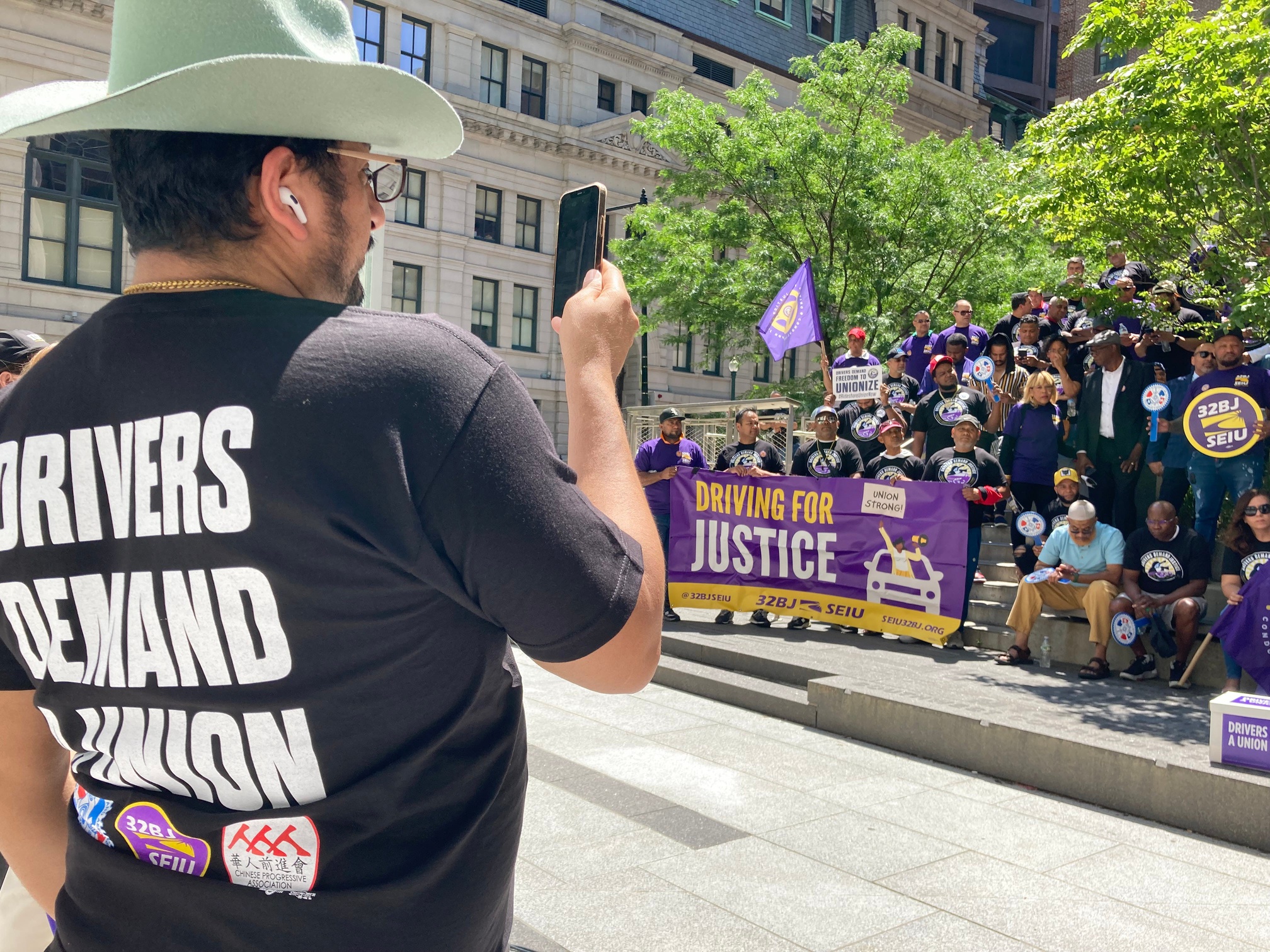 This 2024 file photo shows Denis Rubio, an East Boston Uber driver, record the speeches and chants of dozens of rideshare drivers who gathered to deliver thousands of signatures to Secretary of State William Galvin Tuesday to ensure their ballot initiative made the November ballot.