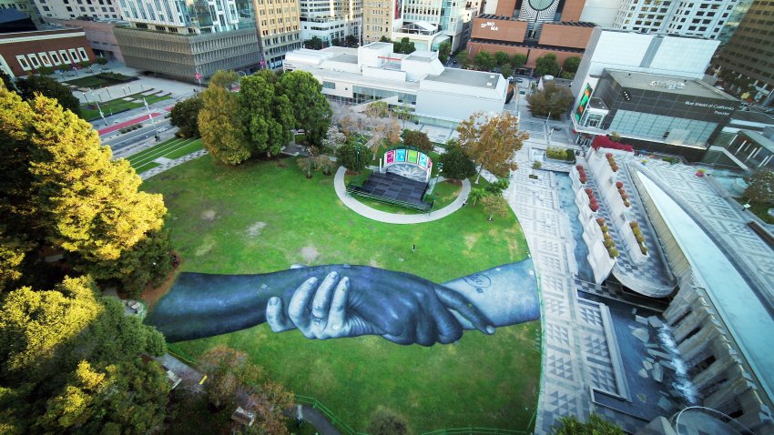 The French-Swiss artist Saype painted an image of locking arms on the lawn of Yerba Buena Gardens as part of a global project he calls Beyond Walls.
